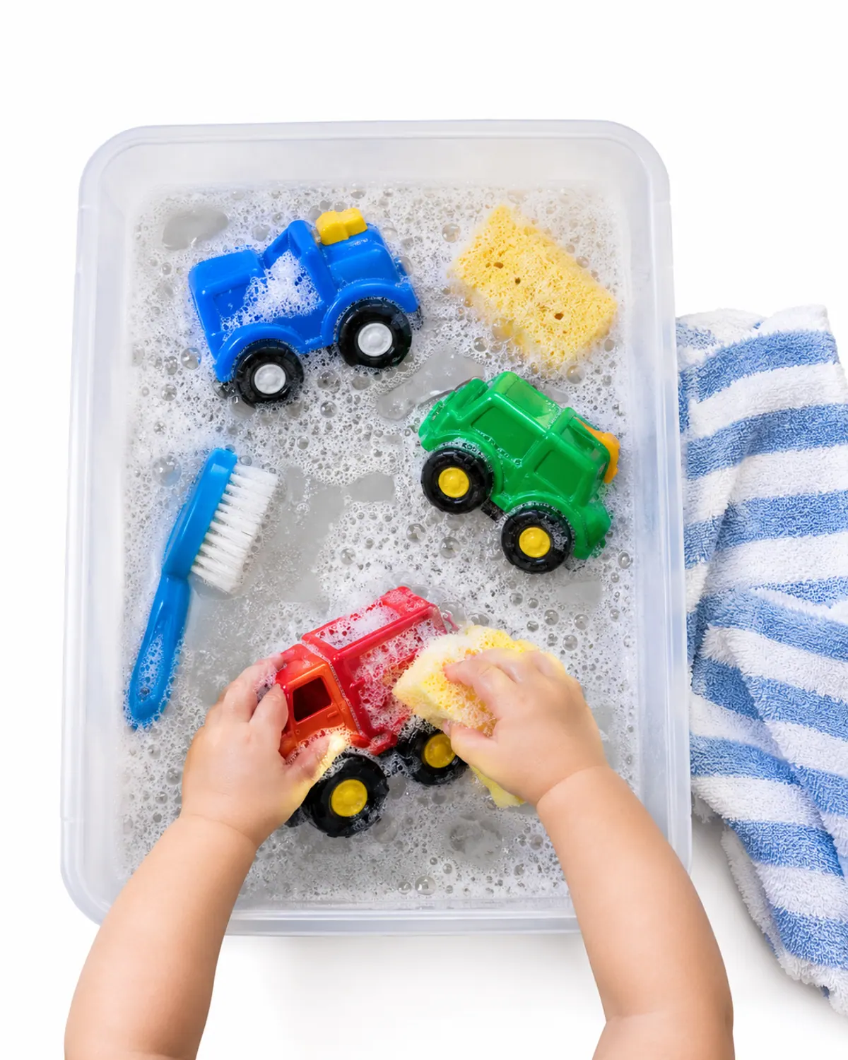 Toddler hands scrubbing a red toy truck with a brush in a bin of soapy water on a patio