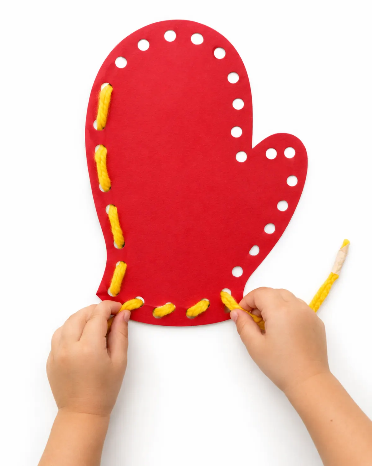 Preschooler hands lacing yellow yarn through hole-punched holes in a red cardstock mitten