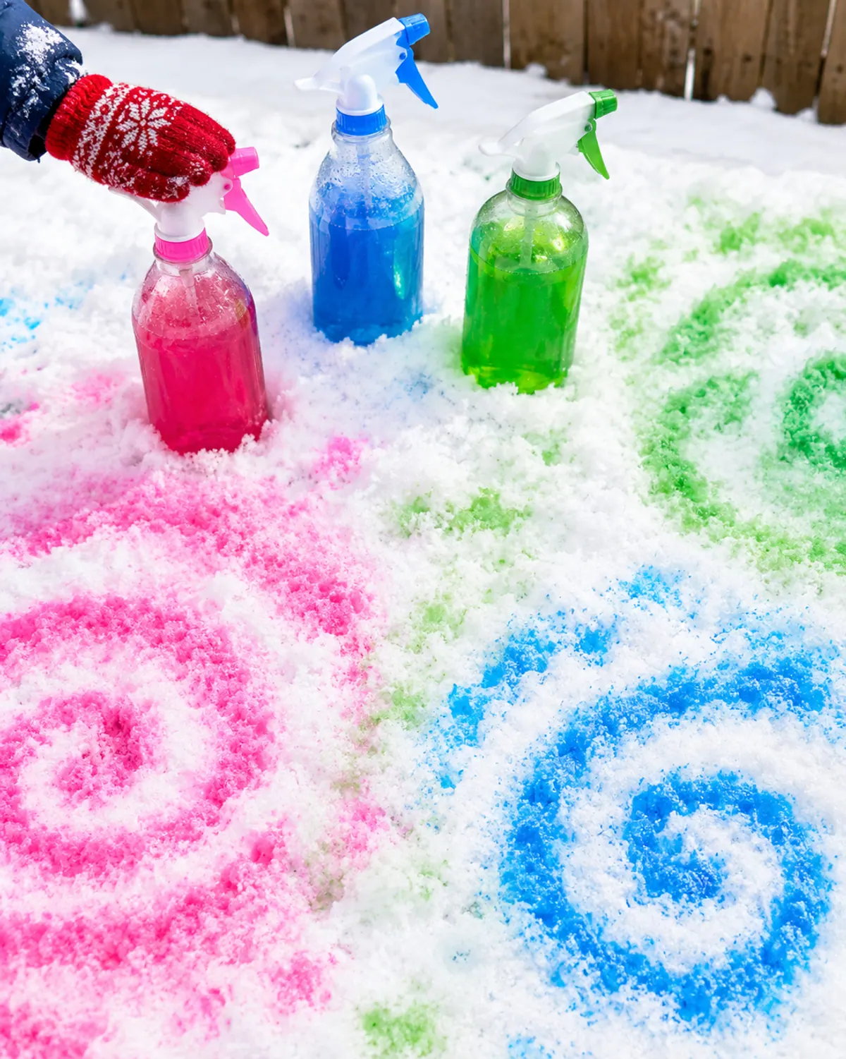 Pink, blue and green colored water sprayed in swirls on fresh backyard snow with three spray bottles